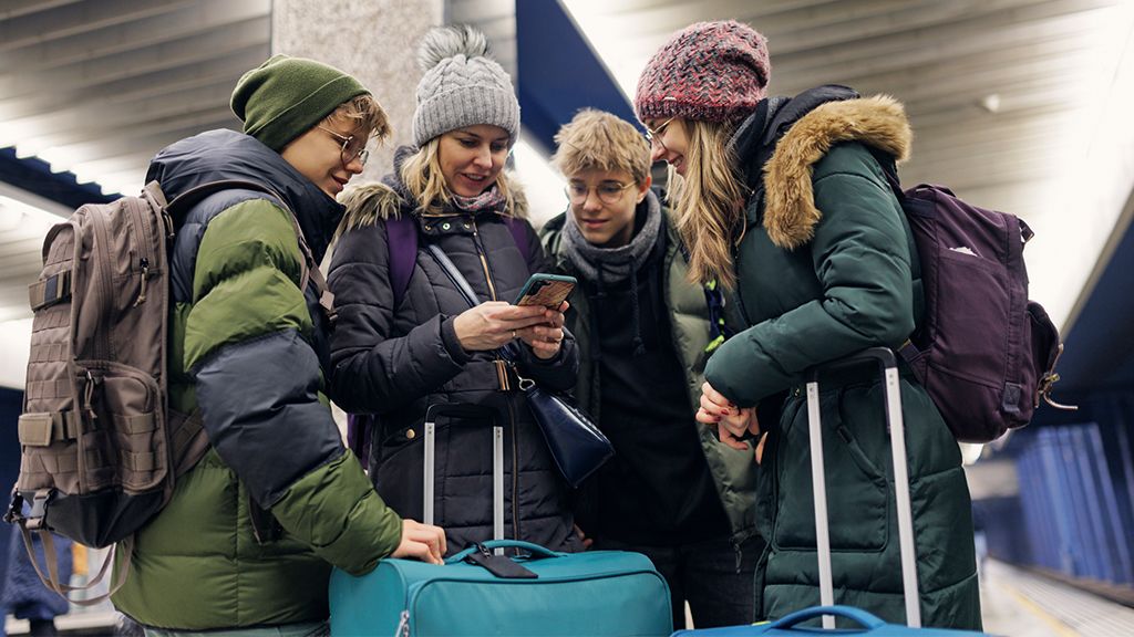 Kobieta z trójką starszych dzieci z walizkami na peronie