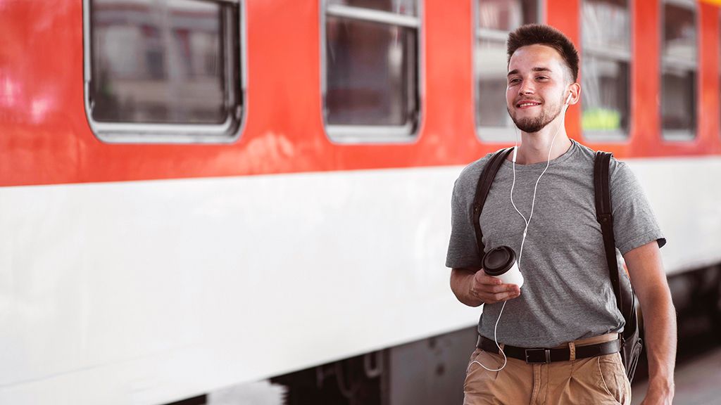 Młody człowiek z kawą w dłoni obok pociągu