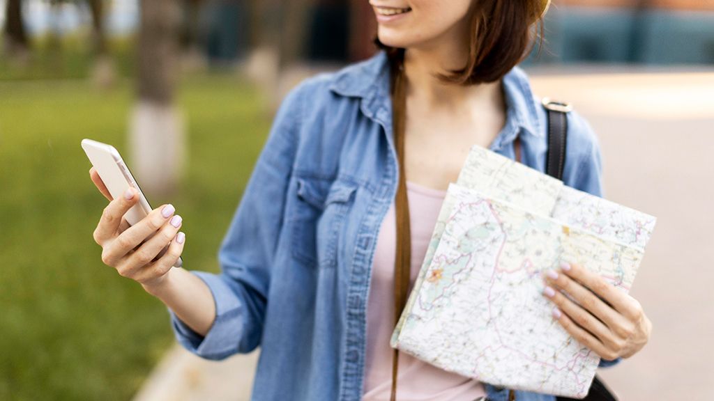 Kobieta trzymająca w dłoniach telefon i mapę