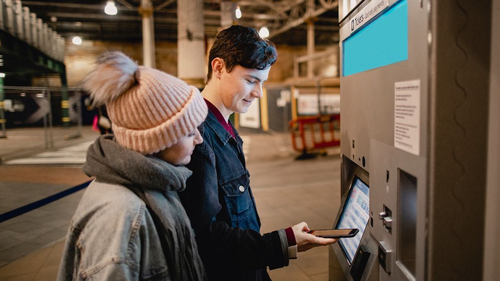 Ludzie kupujący bilet na pociąg w biletomacie - jak kupić bilety kolejowe online