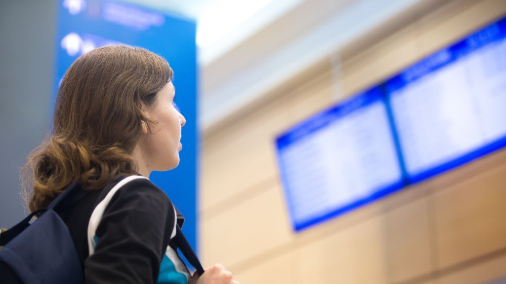 Kobieta stojąca przed tablicą z odjazdami i przyjazdami